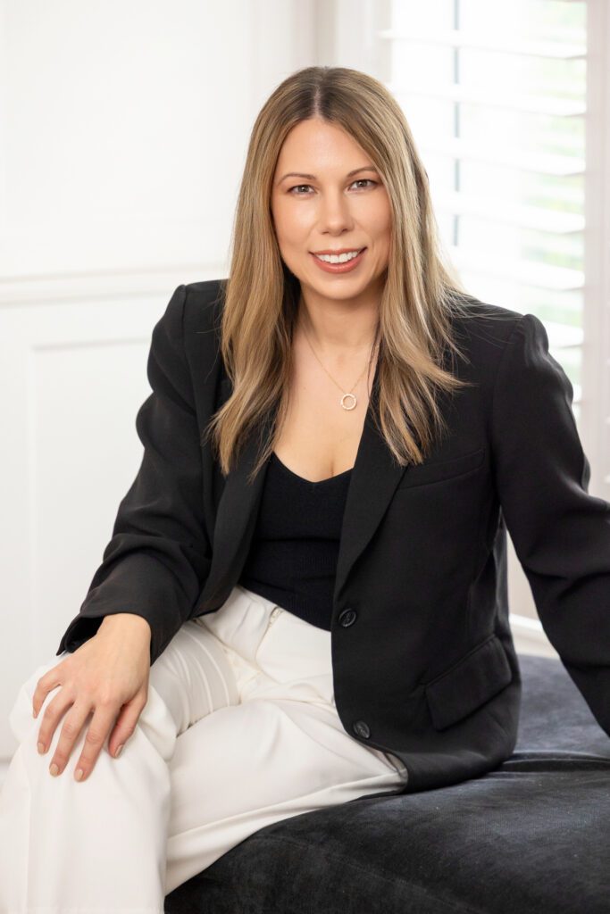 Portrait of a female business owner wearing white pants and a black blazer sitting on a black settee sofa