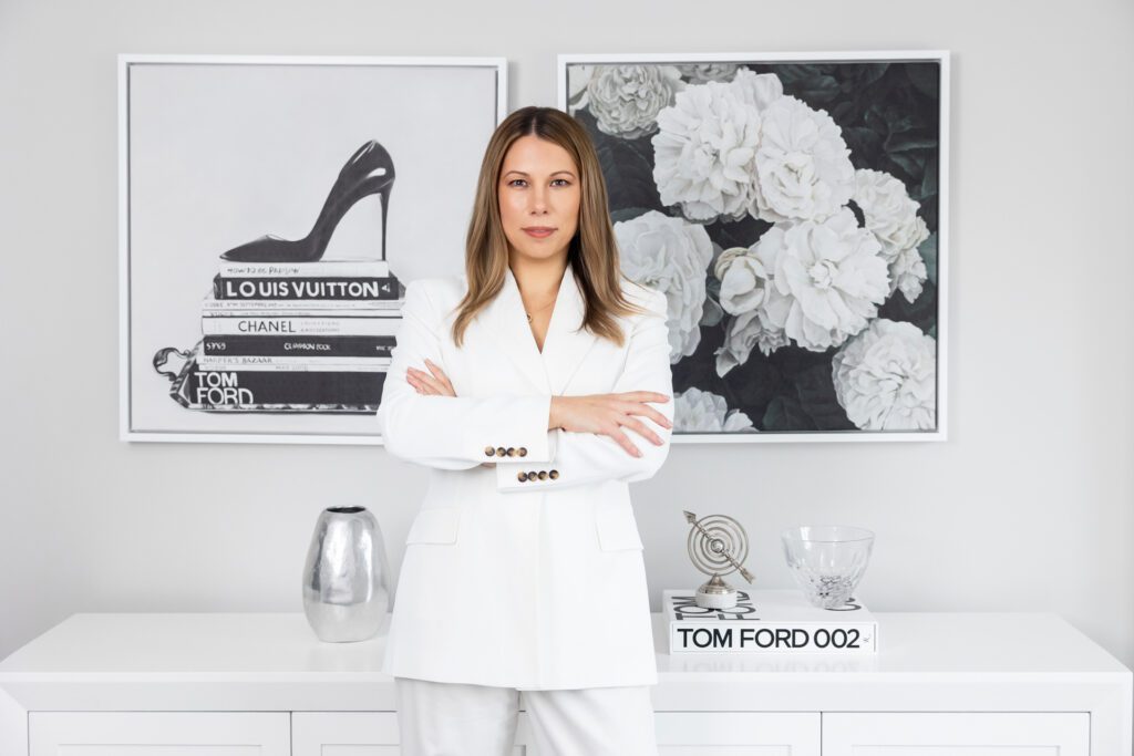 A female business owner wearing a white suit in a power pose with crossed arms standing in front of black and white artwork